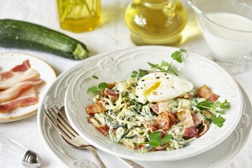 Low-Carb keto carbonara pasta with spaghetti (noodles) of zucchini with cream, fried bacon and poached egg. decorated with pea sprouts. in a beautiful light dish.