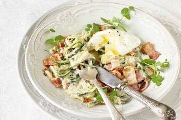 Low-Carb keto carbonara pasta with spaghetti (noodles) of zucchini with cream, fried bacon and poached egg. decorated with pea sprouts. in a beautiful light dish.
