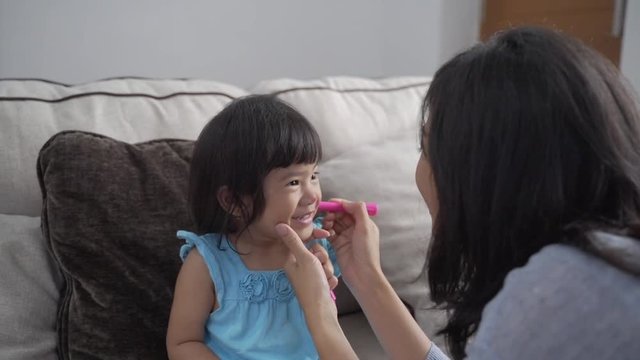 asian mother face painting her little daughter at home. making some cute animal faces