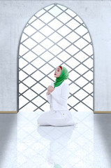 Asian Muslim woman in veil sitting in pray position while raised hands and praying