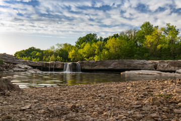 Waterfall at McKinney Falls State Park with large trees and blue sky background, Austin, Texas 