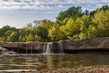 Waterfall at McKinney Falls State Park with large trees and blue sky background, Austin, Texas 