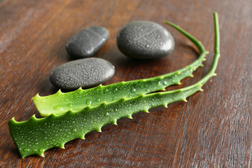 Obraz na płótnie Canvas Fresh aloe vera leaves with spa stones on wooden table