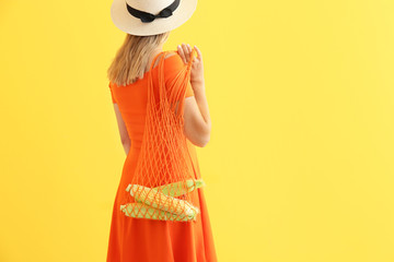 Woman holding mesh eco bag with corn cobs on color background