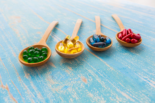 Closeup Colorful Soft Gelatin Capsules Of Food Supplements In Wooden Spoon On Vintage Blue Background