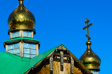 Fototapeta na wymiar Yakut patterns under the roof of the Orthodox Church with Golden domes and crosses made of wood against the blue sky.