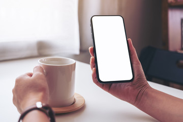 Mockup image of a woman holding black mobile phone with blank desktop screen while drinking coffee