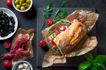 Sandwich with jamon, feta cheese and arugula on a black background top view