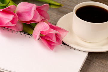 morning coffee in white porcelain cup and spring pink tulips bouquet over rustic wooden table