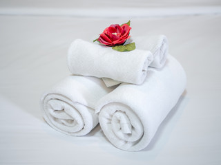White clean towels decoration with red flower on white clean bed in hotel room.