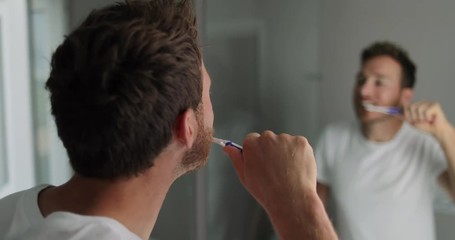 Brushing teeth man looking in mirror of home bathroom using toothbrush in morning routine for clean dental oral care. 4K (UHD) 59.94 FPS SLOW MOTION.