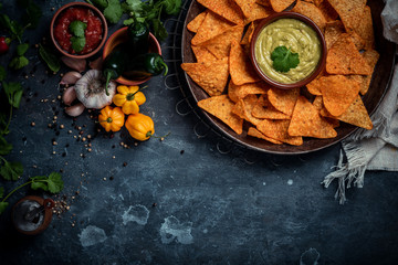 Tortilla chips with guacamole dip, pepper sauce, peppers and koriander