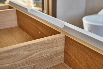 Opened wooden drawer of bathroom vanity in luxury bathroom with teak floor. Stylish interior of...