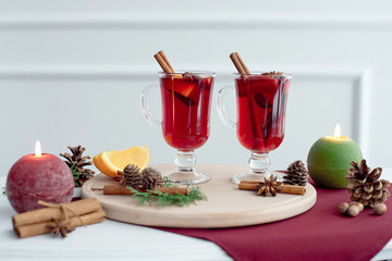 Christmas hot mulled wine with cinnamon, cardamom and anise on a white wooden background. Christmas table with hot drink, candles and wooden tray.