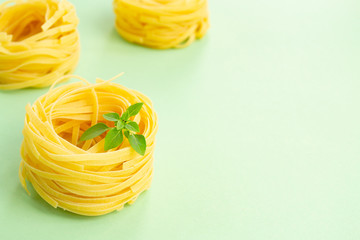 Traditional Italian fettuccine pasta and basil on a light green background. Space for text.