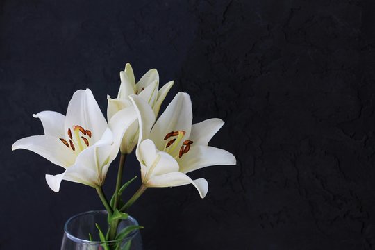 White lily flowers bouquet on black background. Condolence card concept. Close-up, copyspase.