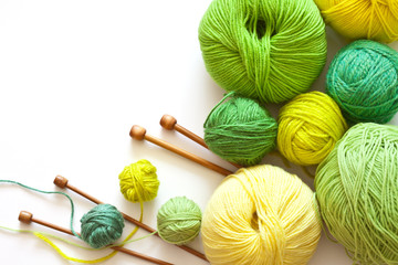 Colorful green balls of yarn for hand knitting and wooden needles on a white background. On left...
