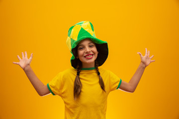 Football supporter, Brazil team. World Cup. Beautiful little girl cheering for her team on yellow background