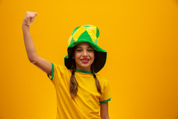 Football supporter, Brazil team. World Cup. Beautiful little girl cheering for her team on yellow background