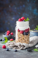 Granola Parfait with Yogurt, oat granola, fresh berries, honey and mint leaves in tall glass jar, copy space