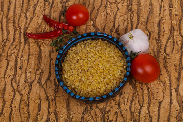 Raw bulgur in the bowl with tomatoes and garlic