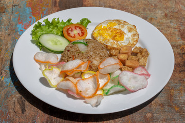 Fried rice with vegetables, rice chips, cheese tofu and fried egg on the old wooden table in local cafe, close up indonesian cuisine. Breakfast in Bali, Indonesia