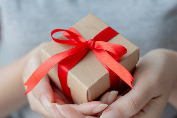 Close up of woman hand holding small brown gift box wrapped with red ribbon.Shallow depth of field with focus on the little box. 