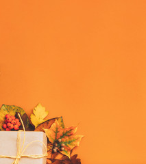 Autumn holiday greeting card. Orange background with cropped beige paper gift box and foliage. Copy space.