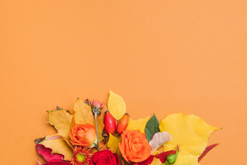 Fototapeta na wymiar Autumn floral bouquet. Fall berries, colorful leaves and roses on orange background. Copy space.