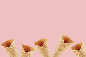Summer food decorative border of empty waffle ice cream cones on soft light pink background, copy space.