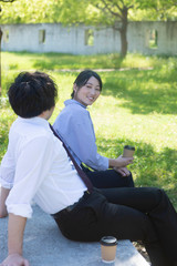 Fototapeta premium 公園で休憩する男女人物,日本,日本人,アジア人,東洋人 ,屋外,春,晴れ,2人,20代,若い,若者,男性,男の人,大人,成人,青年,女の人,女性,男女,ビジネスウーマン,ビジネスマン,上司,部下,同僚,ビジネスパートナー,仕事,ビジネス,ライフスタイル,コピースペース,ポートレート,公園,緑,木,木漏れ日,植物,オフィス街,スーツ,ネクタイ,ビジネスカジュアル,休憩,コーヒーブレイク,コーヒー,飲