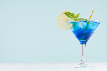 Bright summer fresh blue fruit cocktail with blue curacao liquor, ice cubes, lemon slice, green...