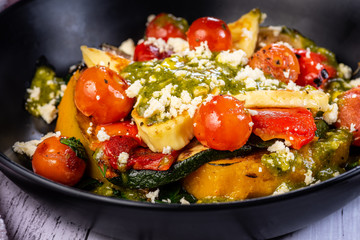 A bowl of roasted vegetables including grilled halloumi cheese and pesto, placed on a white table