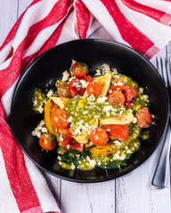 A bowl of roasted vegetables including grilled halloumi cheese and pesto, placed on a white table