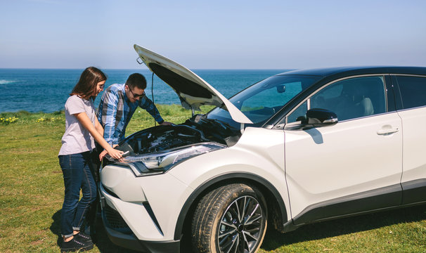 Young couple tries to fix the broken down car near the coast - Powered by Adobe