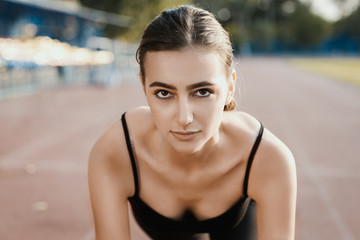 Fototapeta na wymiar Portrait of young sporty woman in sport dress who are ready to run and stands on start on stadium track