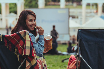 woman eating chips sitting in camp-chair looking movie in open air cinema