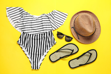 Flat lay composition with striped swimsuit and beach accessories on yellow background