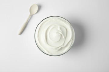 Glass bowl of sour cream and spoon on white background, top view