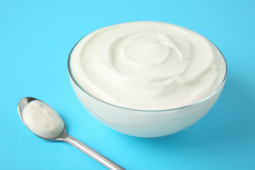 Fototapeta na wymiar Glass bowl of sour cream and spoon on light blue background