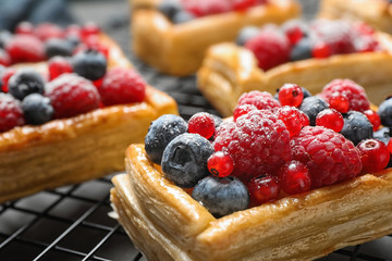 Cooling rack and fresh delicious puff pastry with sweet berries on grey table, closeup