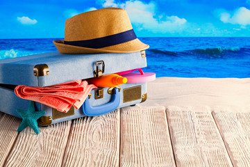 Fototapeta na wymiar Suitcase full of holiday items - summer hat; tanning oil, towel and flip flops on sea background