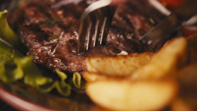 Close up of a knife cutting grilled Balkan cevapi minced meat sausages on a plate in a traditional restaurant setting.