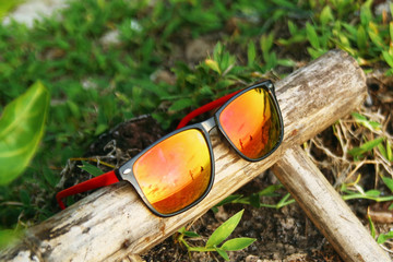 Colorful sunglasses with reflection of sea, beach, trees and sunset sky on a wooden stick.