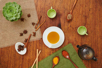 High angle view of cup of green tea on wooden table with teapot and spoons with spices