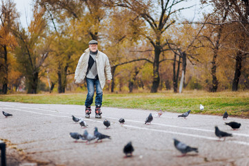 An elderly original man has fun skating on roller skates. People and pigeons. Happy pension. Active...