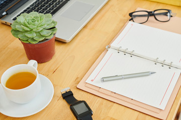 Close-up of opened notepad with blank sheets cup of tea and laptop computer on wooden table at office