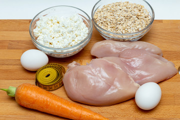 raw chicken breast, cereals, eggs, measuring tape, farm cottage cheese carrot close up on wooden background protein healthy diet fat free concept eco product sports nutrition