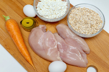 raw chicken breast, cereals, eggs, measuring tape, farm cottage cheese carrot close up on wooden background protein healthy diet fat free concept eco product sports nutrition