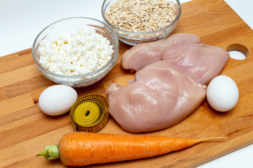 raw chicken breast, cereals, eggs, measuring tape, farm cottage cheese carrot close up on wooden background protein healthy diet fat free concept eco product sports nutrition
